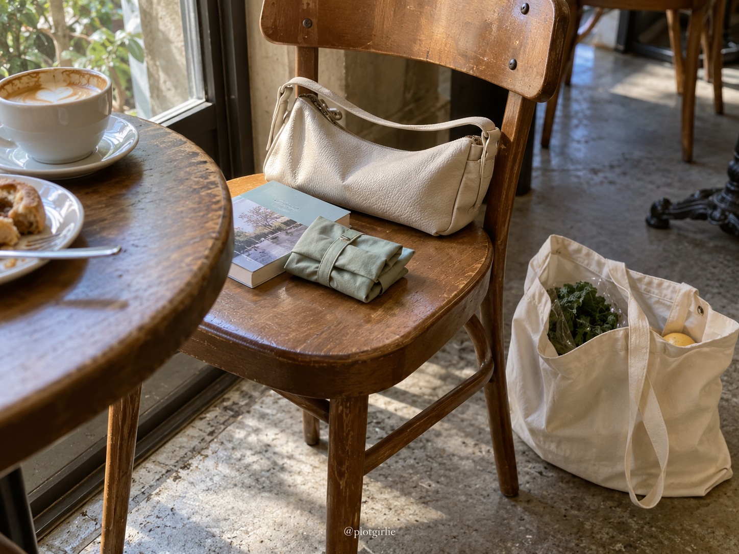 A folded reusable bag and paperback beside a small café bag, with groceries in a tote on the floor