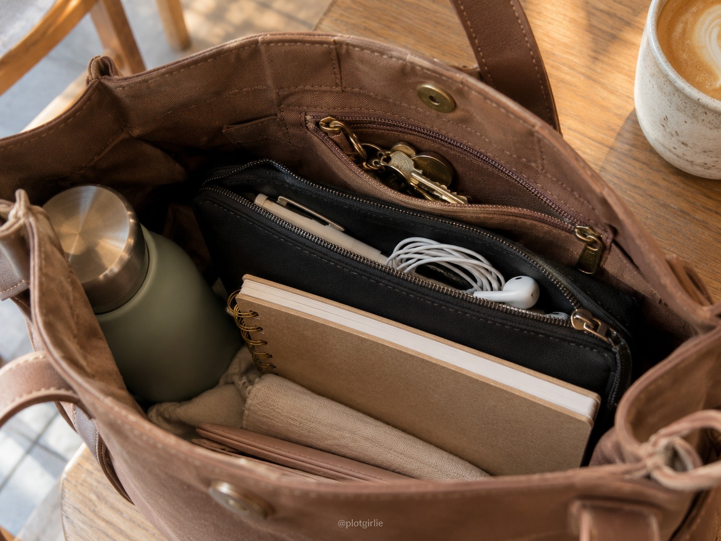 A small black pouch with a pen and earbuds inside a brown bag with accessible keys