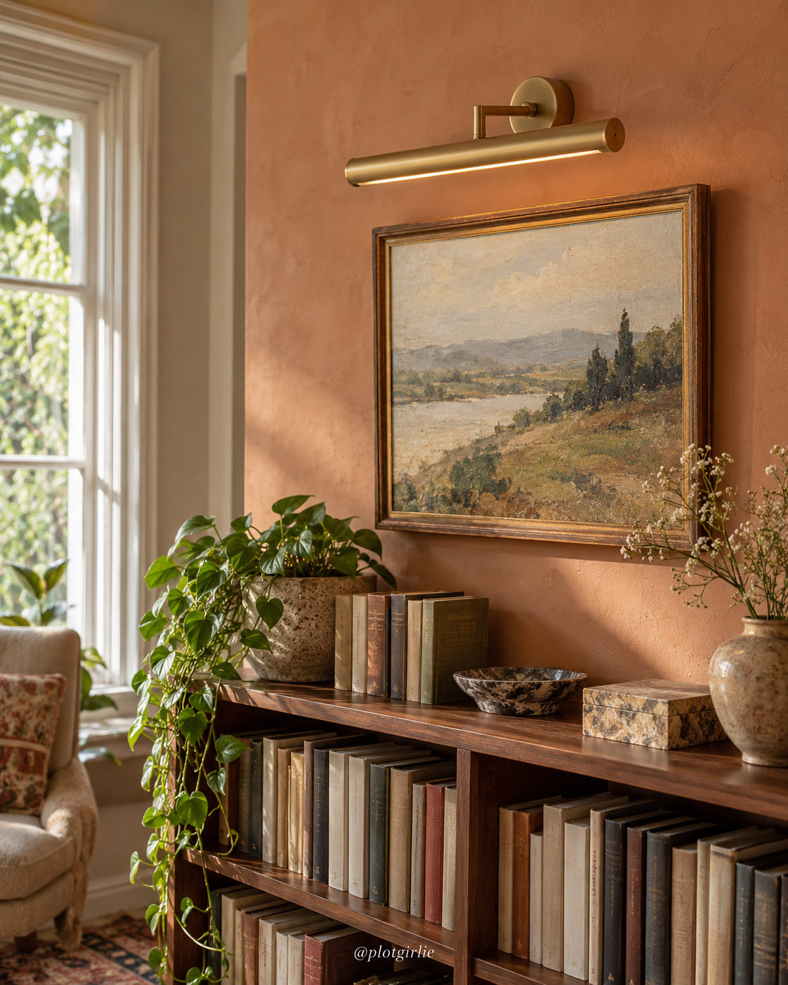 Slim brass-style picture light above framed art beside a bookcase in soft natural daylight