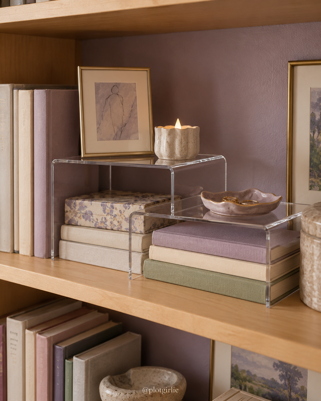 Clear acrylic shelf risers displaying a small framed drawing and an unlit decorative candle